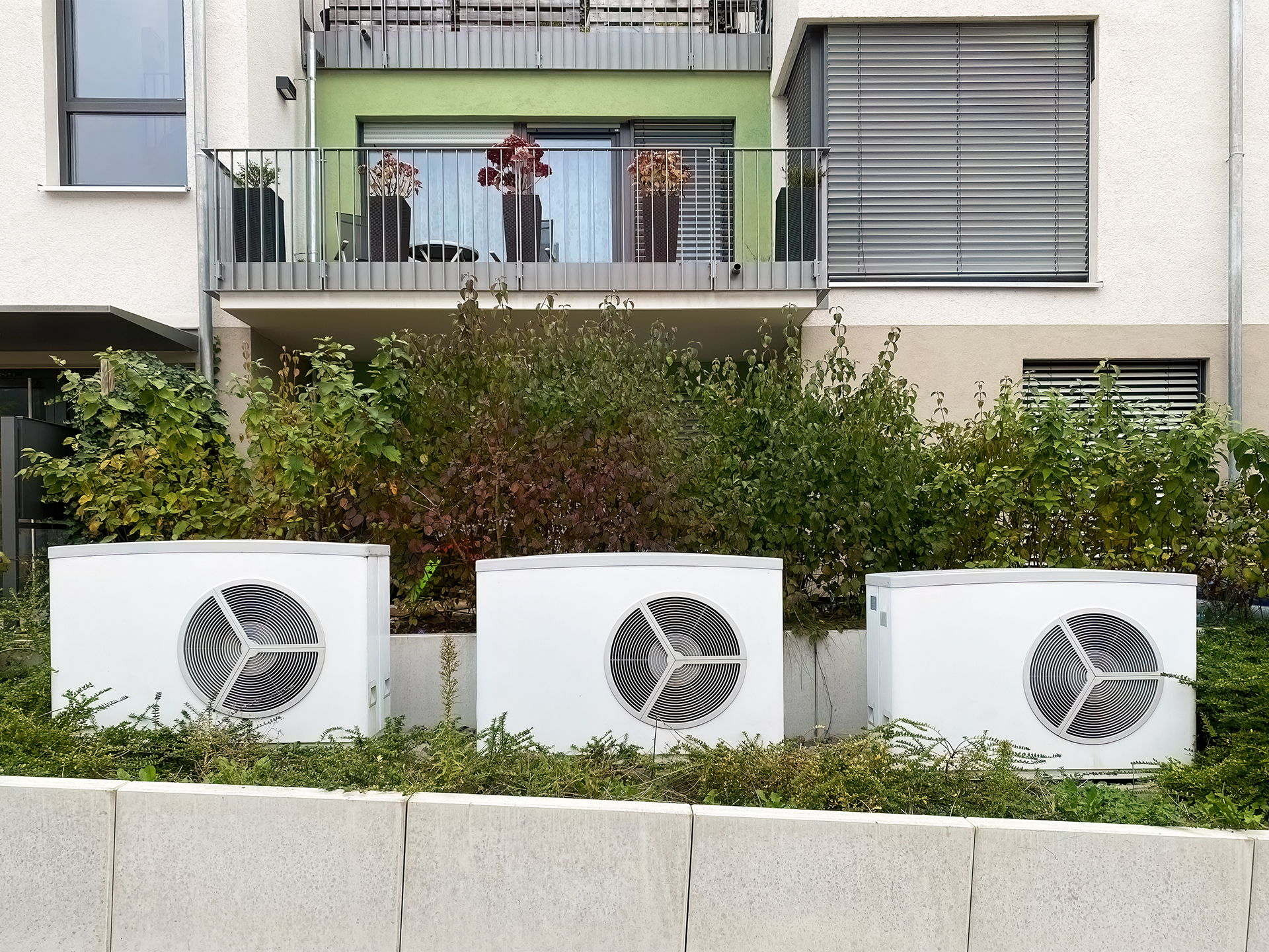 Mehrere Wärmepumpen vor einem Mehrfamilienhaus.